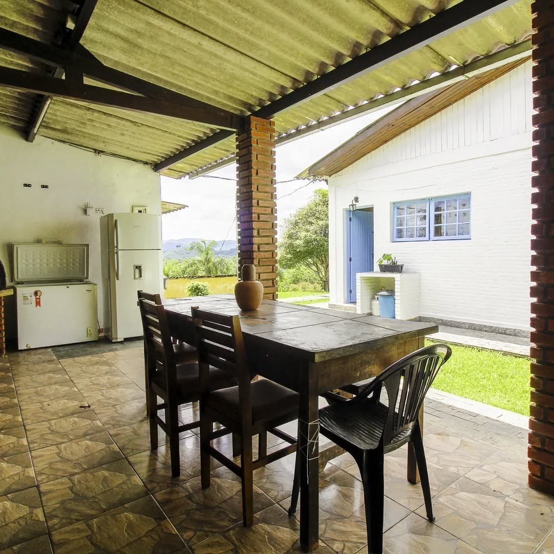 Mesa de jantar na área gourmet coberta, com a casa e o jardim ao fundo
