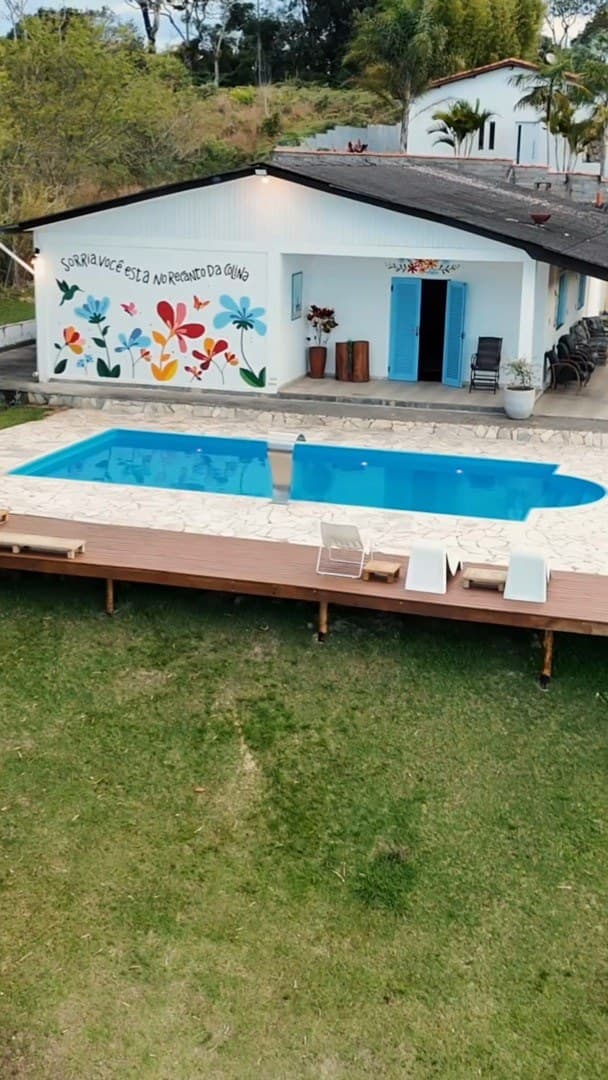 A casa branca com o mural de flores e a piscina vistas do alto, de frente