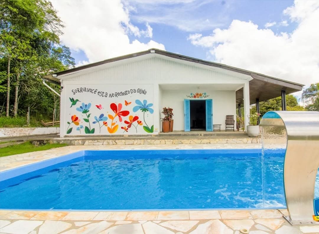 Fachada da casa com o mural de flores e beija-flor, e a piscina em frente
