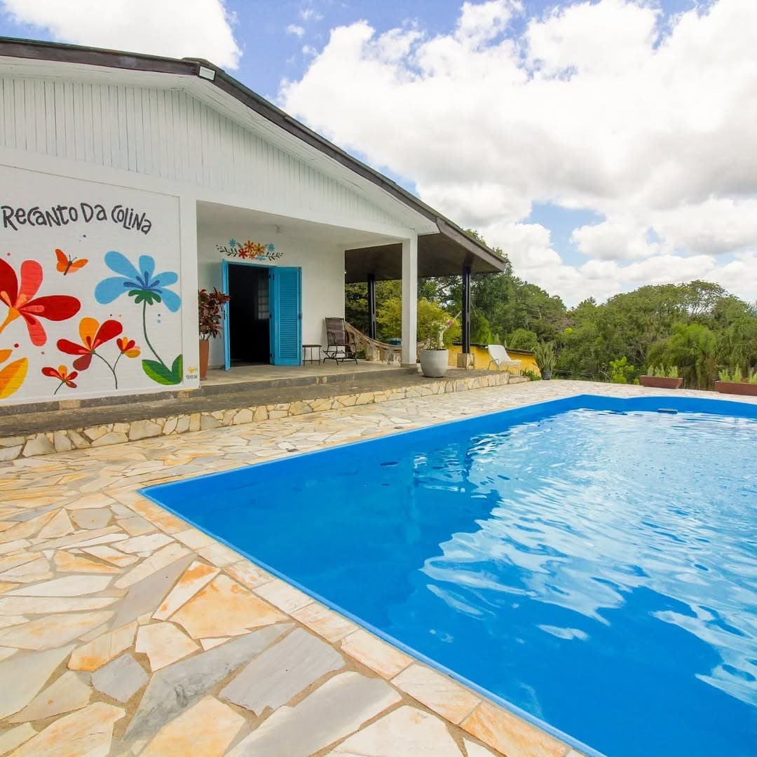 A casa branca com janelas azuis e o mural de flores coloridas, ao lado da piscina