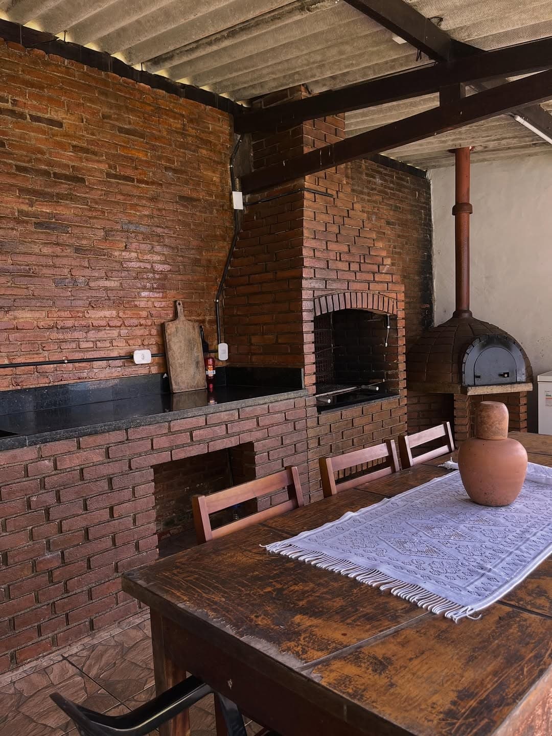 Área gourmet de tijolos com churrasqueira, forno de pizza e mesa de madeira