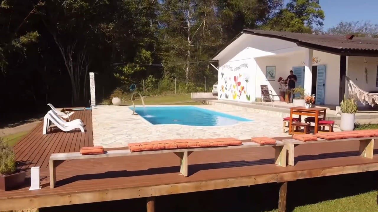O deck de madeira contornando a piscina, com a casa e o gramado em declive