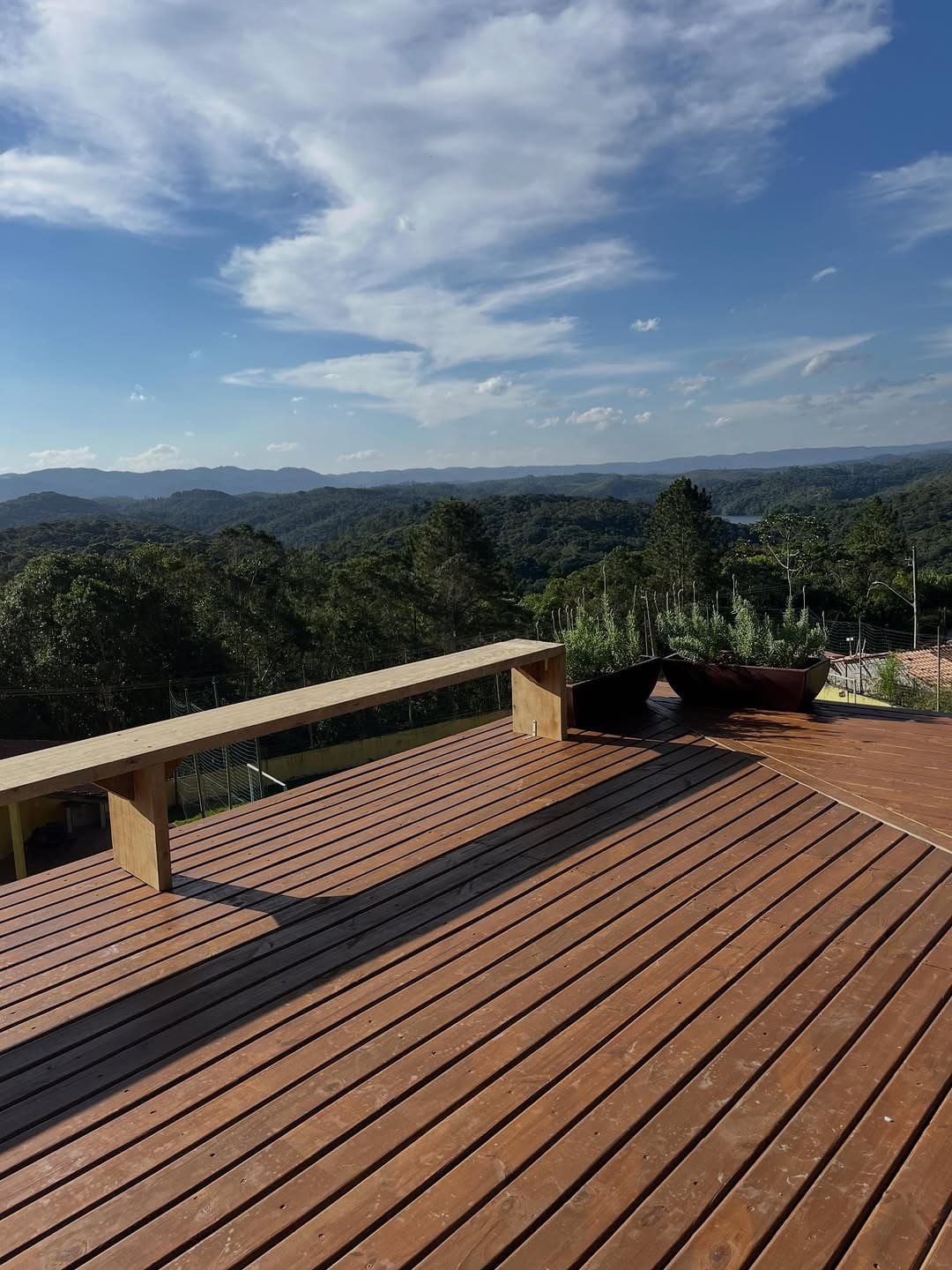 Deck com bancos de madeira e floreiras, sob céu azul