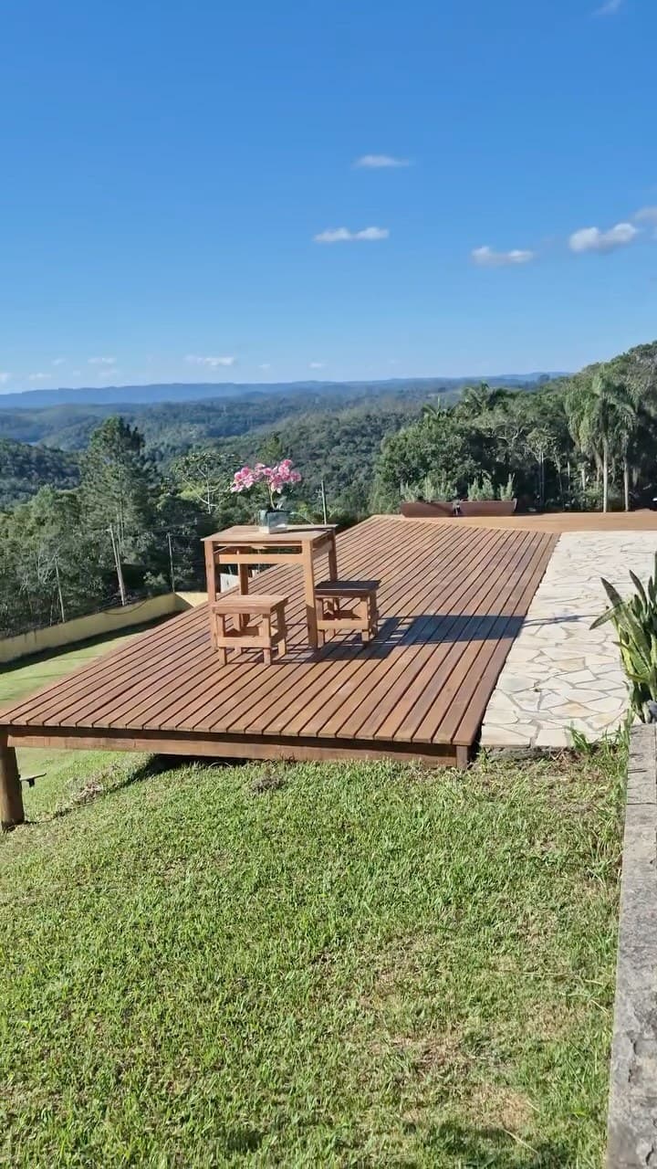 Mesa e bancos no deck com um vaso de flores, de frente para o vale