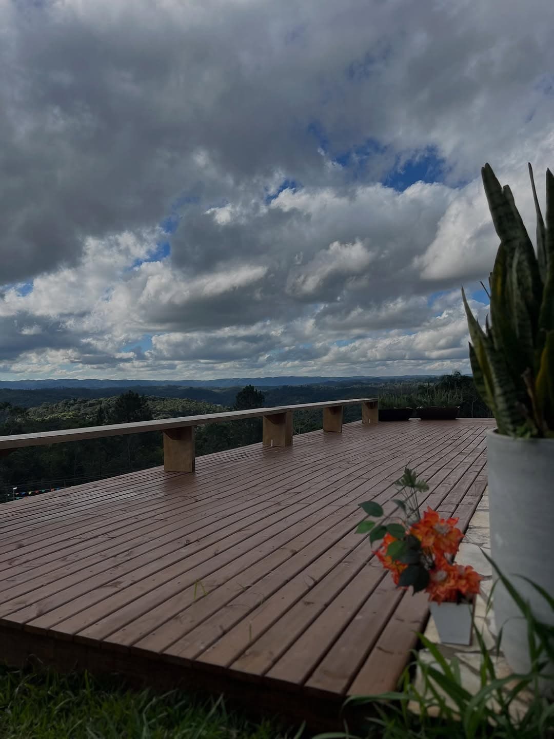 O deck de madeira sob um céu de nuvens, com a vista da serra