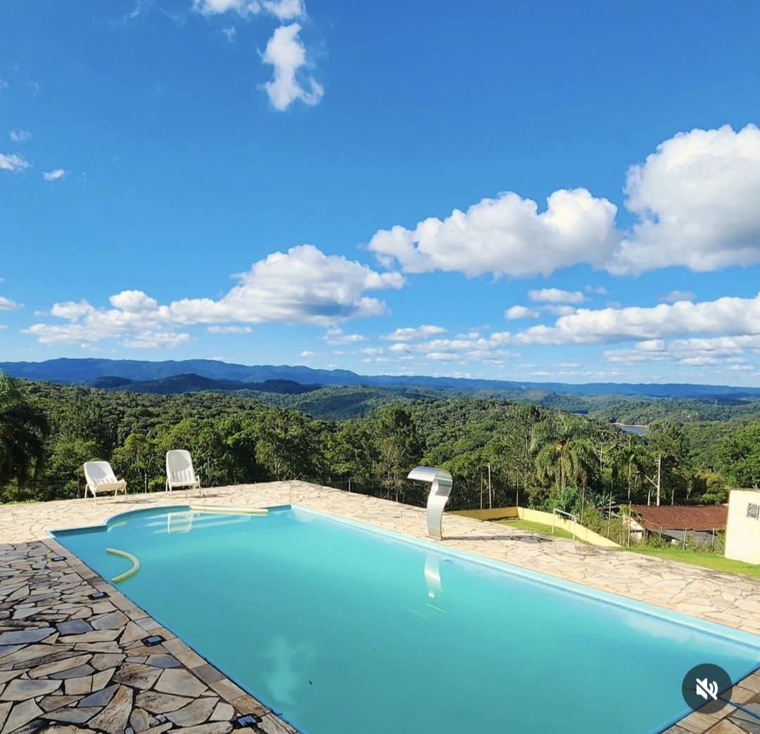 Piscina azul com piso de pedra e a vista das serras sob um céu de nuvens