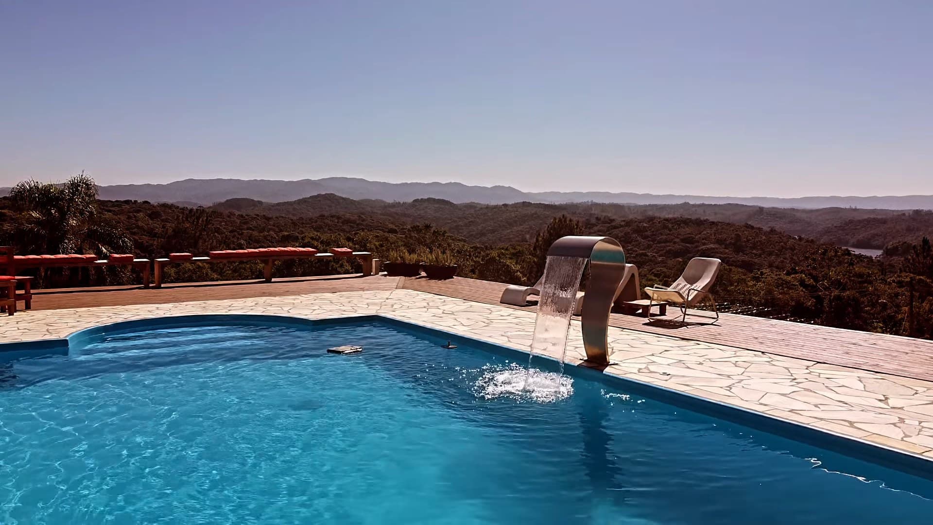Piscina, espreguiçadeiras e o deck com a vista das montanhas ao fundo