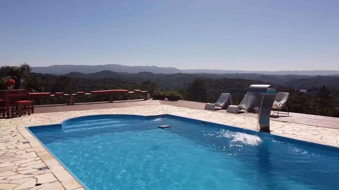 Piscina com cascata e piso de pedra, com as serras no horizonte