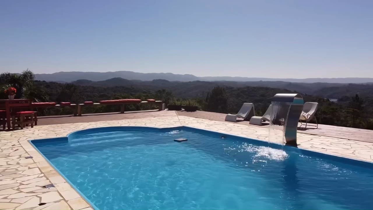 Piscina com cascata e piso de pedra, com as serras no horizonte