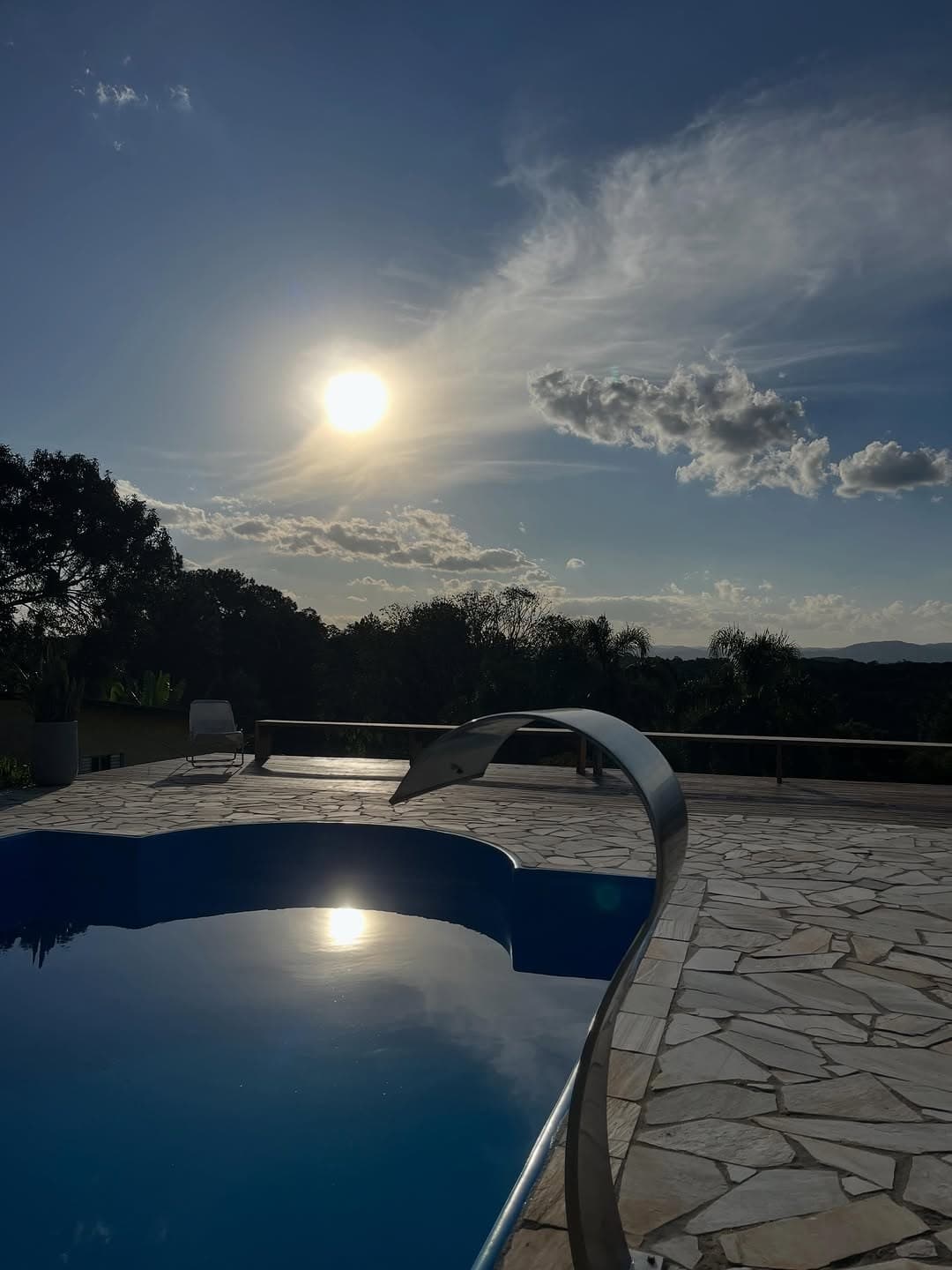 O sol refletido na piscina ao entardecer, com a cascata em silhueta
