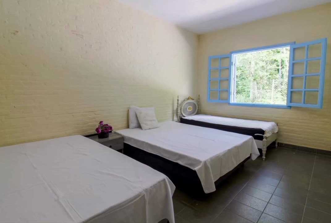 Quarto com camas de solteiro e janela azul aberta para a mata