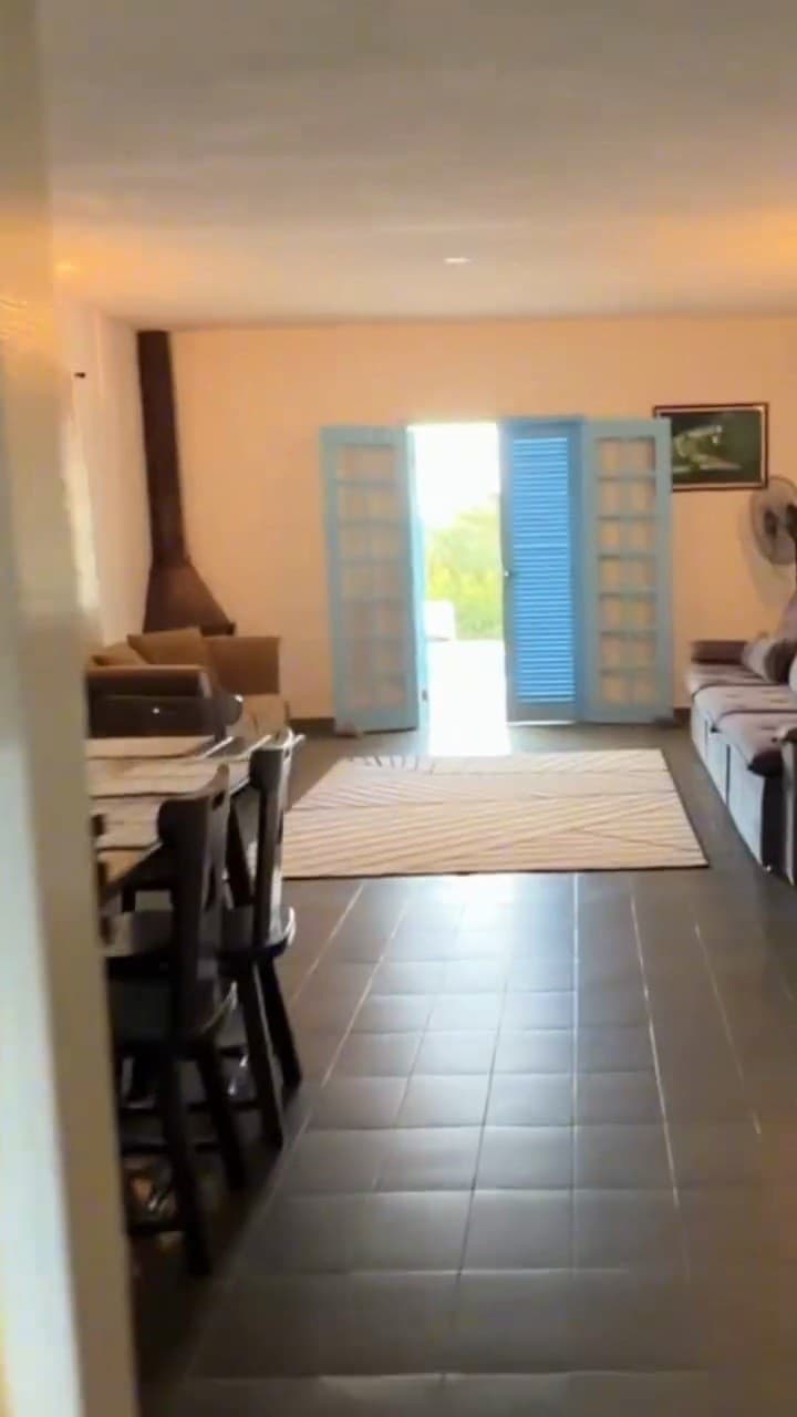 A sala vista de ponta a ponta, com a lareira e a porta para a varanda