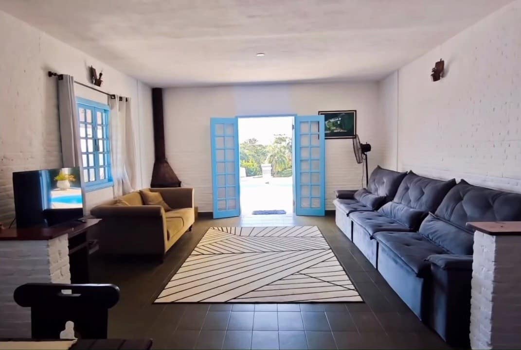 Sala ampla com sofás, Smart TV e a porta azul aberta para a piscina